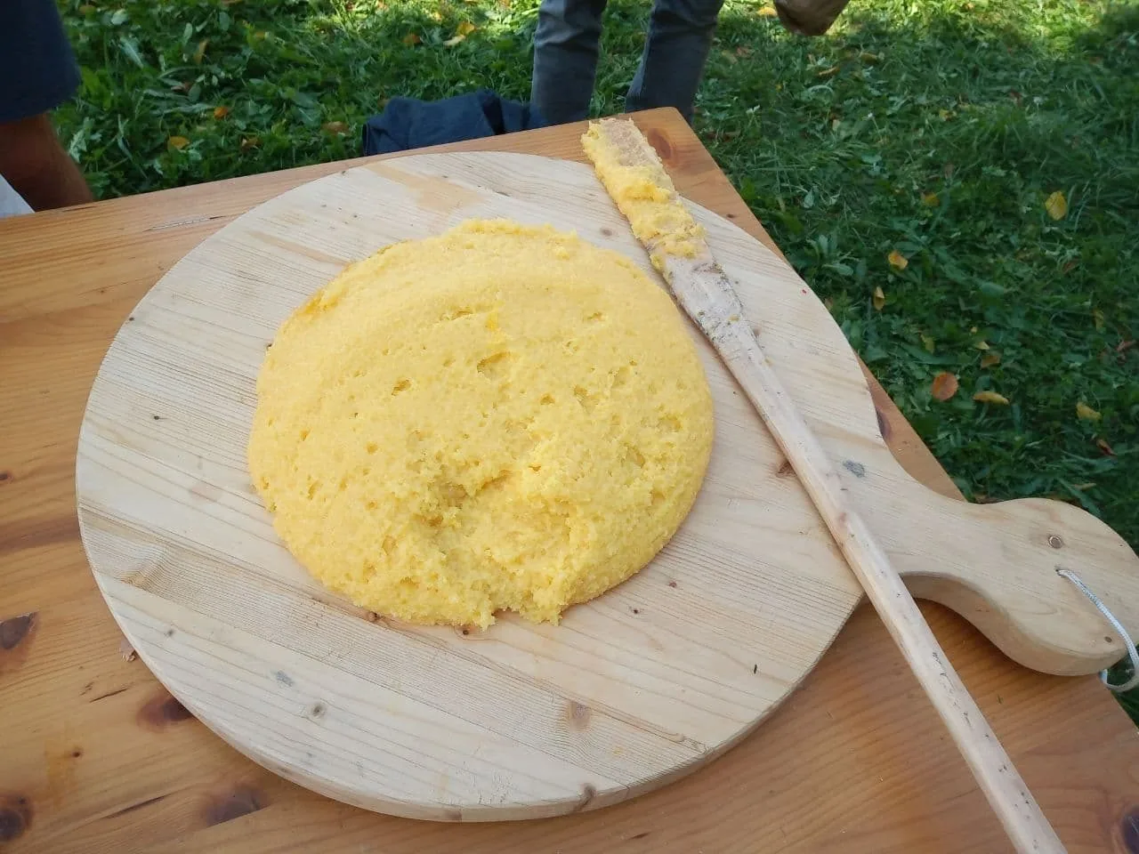 Polenta gialla appena rovesciata su un tagliere di legno con il mestolo, servita all'aperto su un prato