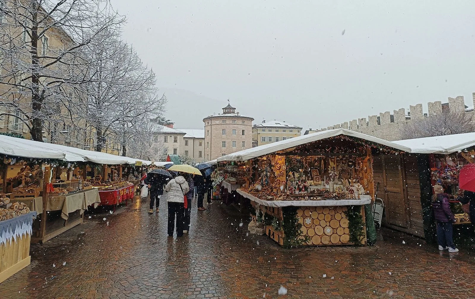 Le casette di legno del mercatino di Natale in piazza Fiera a Trento sotto la neve, con le mura medievali sullo sfondo