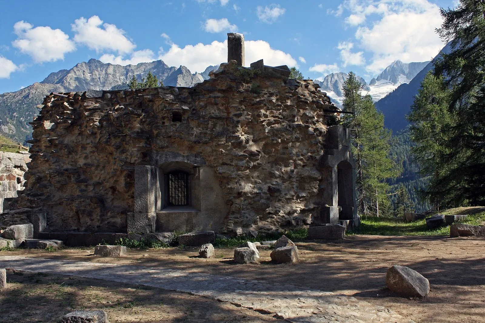 Le mura in pietra del Forte Strino a Vermiglio tra i larici, con le cime della Presanella sullo sfondo